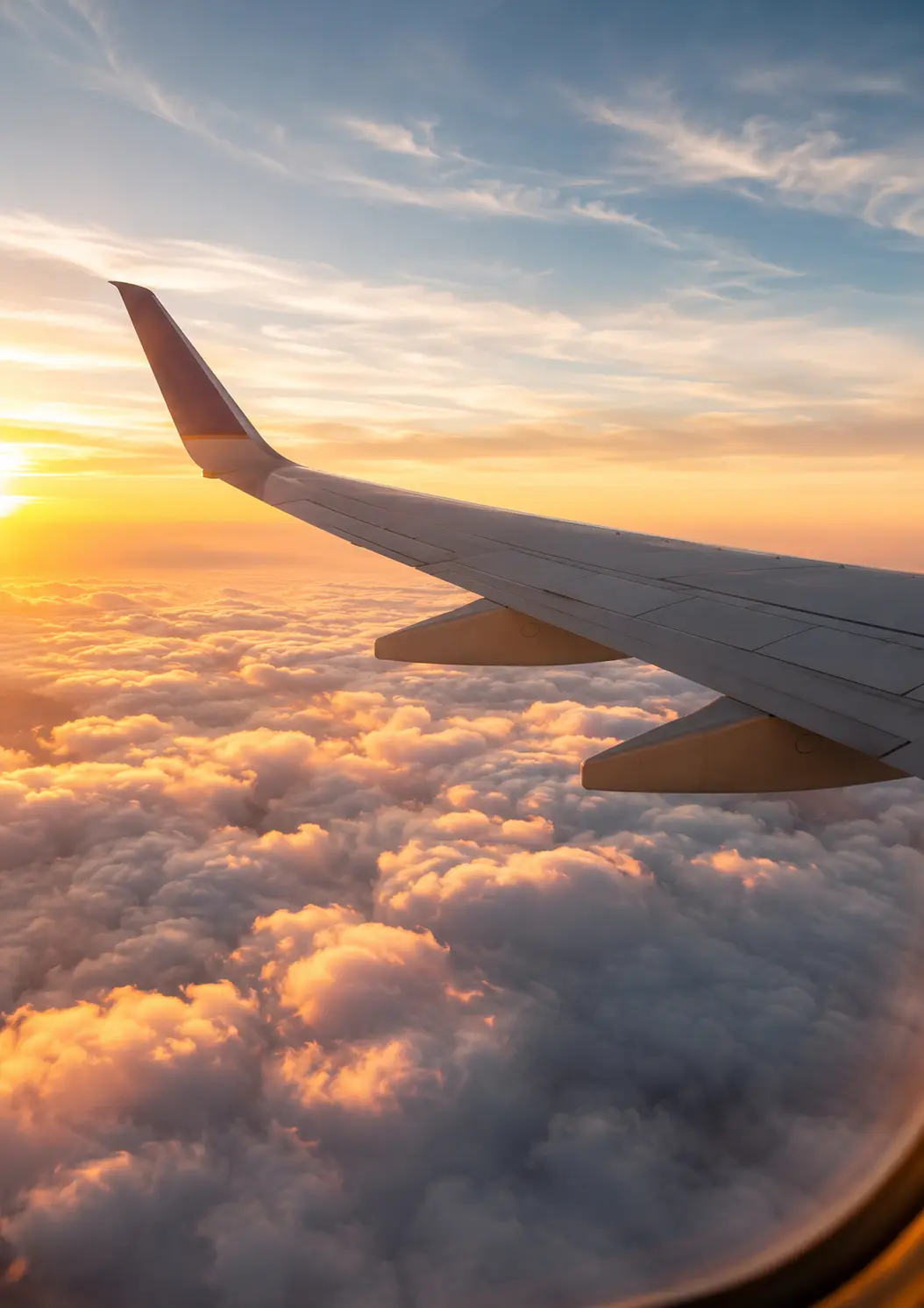 Airplane wing over clouds at golden hour, seen from a window seat